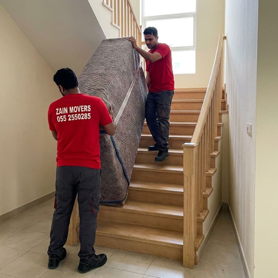 Zain Movers crew carrying a wrapped wardrobe up a JVC townhouse staircase