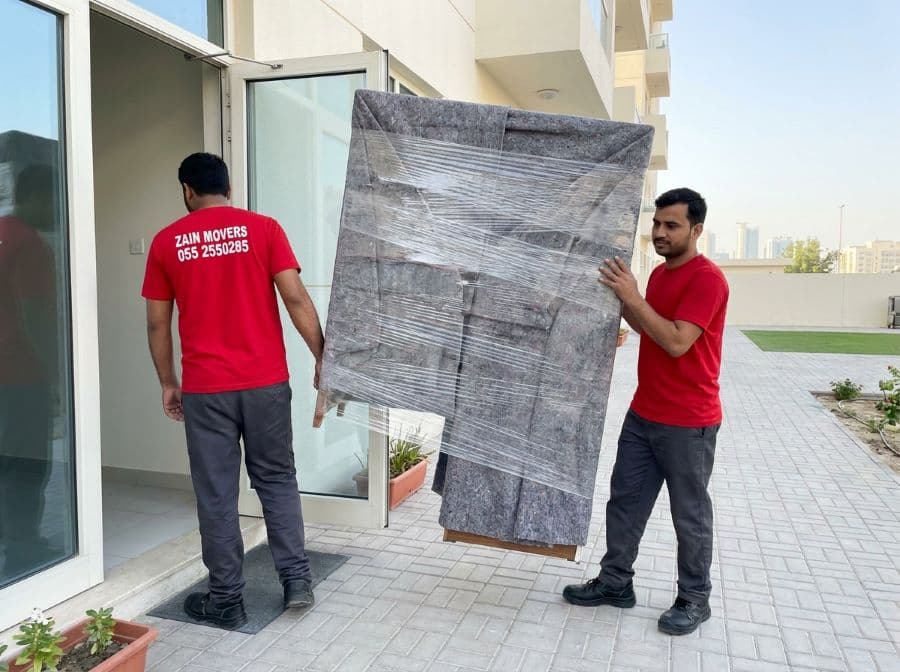 Zain Movers team carrying wrapped furniture into an Ajman apartment building