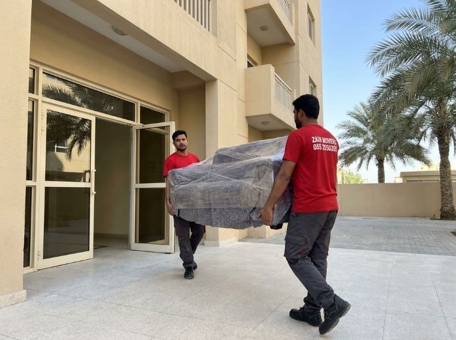 Zain Movers crew carrying wrapped furniture out of a Sharjah apartment building