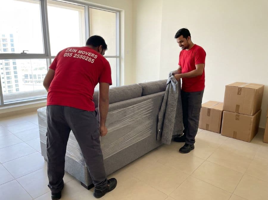 Zain Movers crew wrapping a sofa in protective blankets inside a Dubai apartment living room
