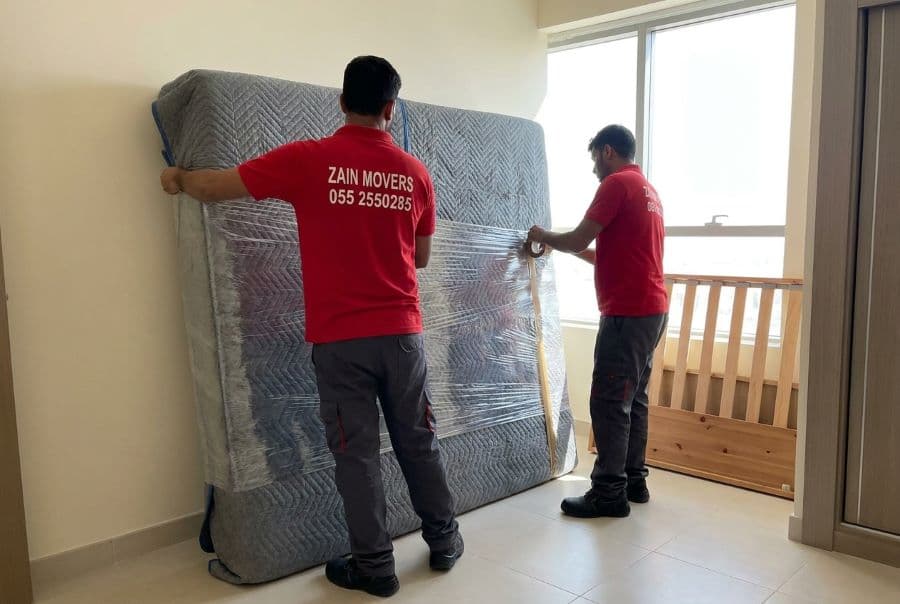 Movers protecting a mattress with heavy blankets and stretch film before loading in Dubai